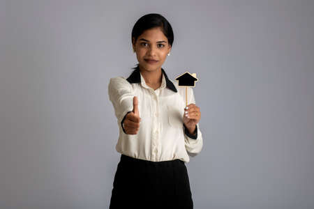 Happy young woman holding a little house cutout board in her hands on a gray background.の写真素材
