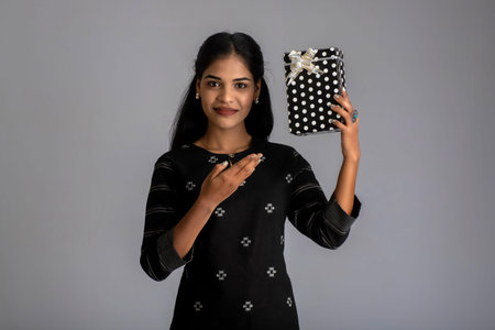 Portrait of young happy smiling woman Girl holding gift box on a grey background.