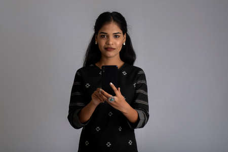 Young Indian girl using a mobile phone or smartphone on gray backgroundの写真素材