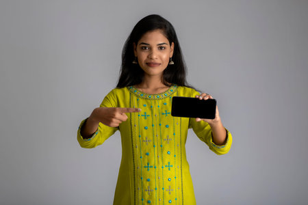 Young beautiful girl holding and showing blank screen of smartphone or mobile or tablet phone on a...
