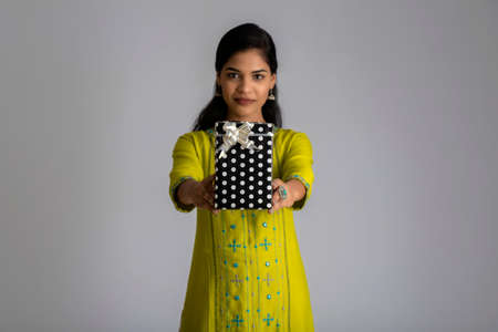 Portrait of young happy smiling woman Girl holding gift box on a grey background.の写真素材