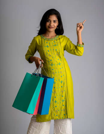 Beautiful young girl holding and posing with shopping bags on a grey backgroundの写真素材