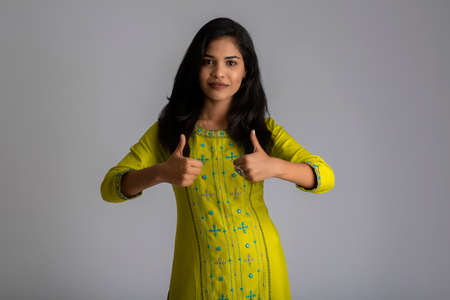 Young smiling girl showing ok sign or thumbs up on a grey backgroundの写真素材