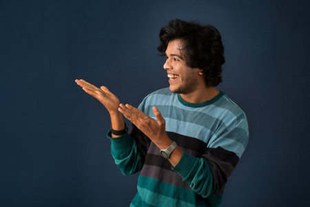 Portrait of a successful cheerful young man pointing and presenting something with hand or finger with a happy smiling face.の写真素材