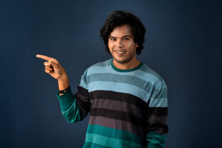 Portrait of a successful cheerful young man pointing and presenting something with hand or finger...
