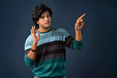 Portrait of a successful cheerful young man pointing and presenting something with hand or finger with a happy smiling face.の写真素材