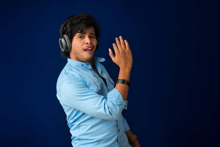 Portrait of a handsome young man enjoying music on headphones on blue background.の写真素材