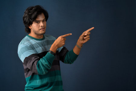 Portrait of a successful cheerful young man pointing and presenting something with hand or finger with a happy smiling face.の写真素材