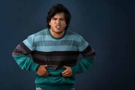 Unhappy man suffering from stomach ache over gray background. People, healthcare, and health problem concept.の写真素材