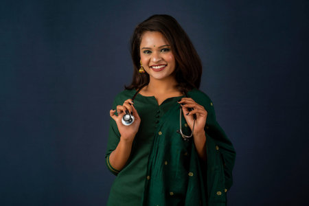 A smiling female doctor wearing a stethoscope on her shoulders looking at the camera on gray...