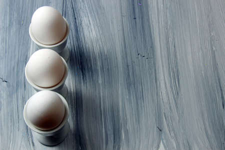 Overhead view of white eggs in egg cups on a textured grey wooden background with copy spaceの写真素材