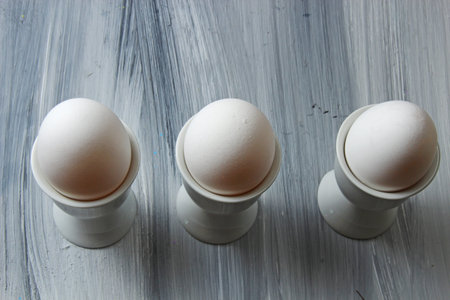 Overhead view of white eggs in egg cups on a textured grey wooden background with copy space.