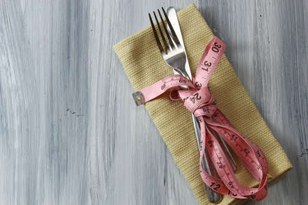 A healthy eating concept of a napkin with fork and knife wrapped up in a measuring tape on a grey textured background with copy space.の写真素材