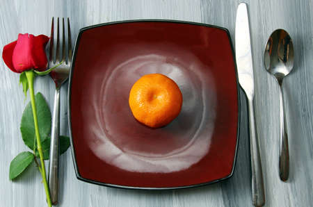 A romantic table setting with a Rose bud and an orange on a rustic wooden textured background.の写真素材
