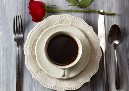 Overhead view of a coffee cup and plate with black coffee and a red Rose.の写真素材