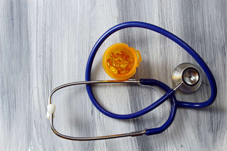 A blue stethoscope with a bottle of pills on a wooden background with copy space.の写真素材