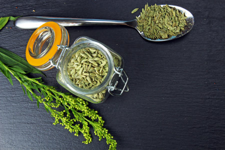 Fennel seeds in a jar on a grey moody background with copy space, selective focus.