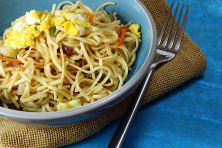 Chinese noodles or chowmien with eggs and veetables in a bowl on blue  background with copy space.の写真素材