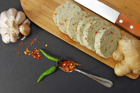 Slices of homemade spicy chicken salami with ginger, garlic, cilantro and red pepper on a moody background with copy space, selective focus.の写真素材