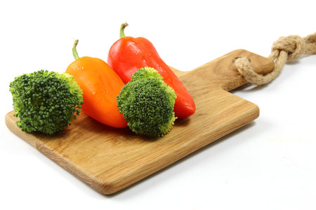 A cutting board with Broccoli, peppers and onions on white background.の写真素材