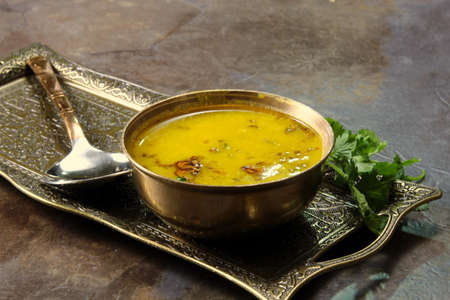 Yellow Lentil soup or Arhar Daal fry with the tadka of cumin seeds, garlic and green chilies in a bowl on a tray with cilantro leaves on the side, selective focus.の写真素材