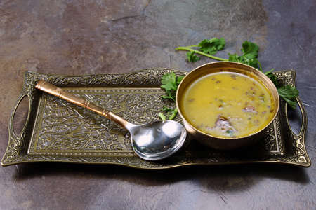 Yellow Lentil soup or Arhar Daal fry with the tadka of cumin seeds, garlic and green chilies in a bowl on a tray with cilantro leaves on the side with copy space, selective focus.の写真素材