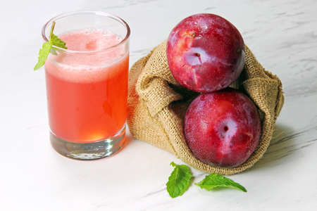 A glass of plum juice with a bag full of fresh plumsの写真素材