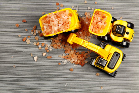 A yellow toy truck on a grey stone background with pink Himalayan salt with copy space,  selective...
