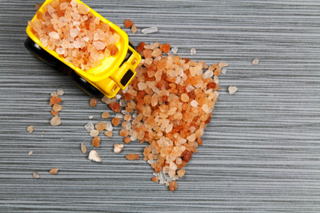 A yellow toy truck on a grey stone background with pink Himalayan salt with copy space,  selective...