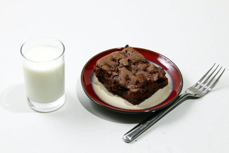 Chocolate brownies with chocolate chips on a plate with a glass of milkの写真素材