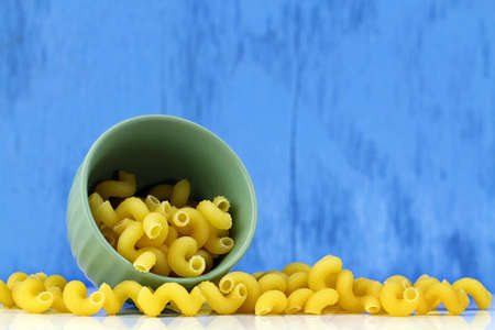 A bowl of cavatappi pasta on a blue bakground, selective focus with copy space.の写真素材