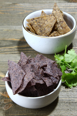 Purple corn chips and bean chips in a bowl with cilantro leaves on a wooden background, selective...