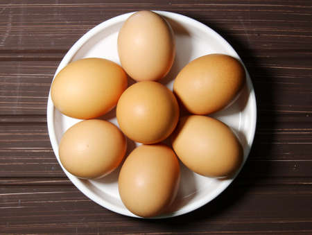 Top view of brown eggs in a white round plate on a wooden backgroundの写真素材