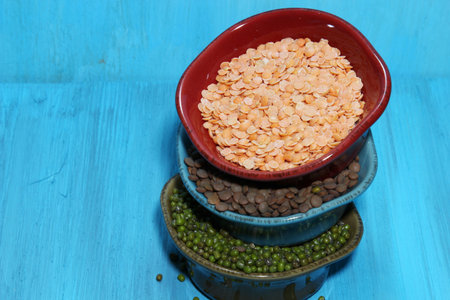 Different kinds of Indian lentils stacked in colorful bowls on a blue wooden backgroundの写真素材