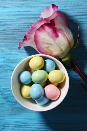 Top view of a bowl of colored Easter candy and a pink Rose on a blue backgroundの写真素材