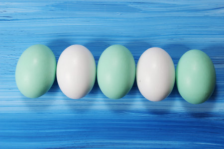 Green and white easter Eggs in a row on a wooden blue background.