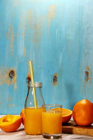 Orange juice with cut up oranges on a blue wooden backgroundの写真素材