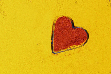 A background of turmeric powdr with a heart shape of parika or red chili powder.の写真素材
