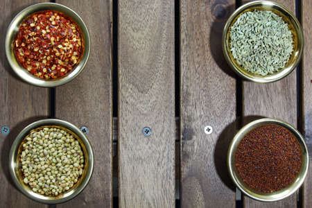 Bowls of spices containing mustard seeds, nigella seeds, fennel seeds, coriander seeds, red pepper flakes, methi seeds on a wooden background.Top view.の写真素材
