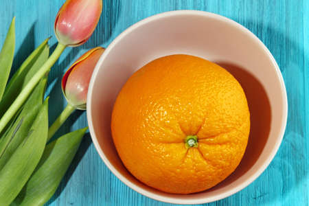 A large Orange in a bowl with fresh Tulips on blue wooden background, selective focus. Top view.の写真素材