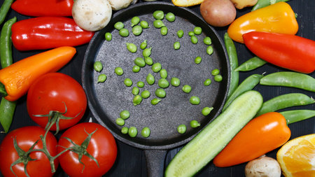 Top view of a cast iron skillet surrounded by vegetables like tomatoes, potatoes, peas, peppers, cabbage and mushroomsの写真素材