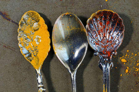 Empty spoons with yellow turmeric powder and traces of Paprika on a rustic dark background.の写真素材