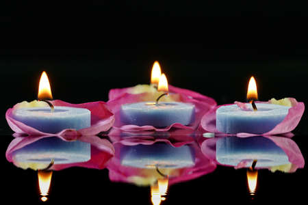 Lighted blue candles on Rose petals and black pebblesの写真素材