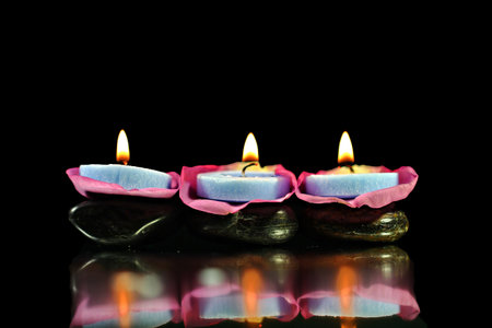 Lighted blue candles on Rose petals and black pebblesの写真素材