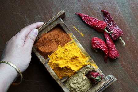 A hand holding a spices box with turmeric powder, coranider powder, and chili powder.の写真素材