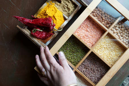 A hand holding a box with different kinds of lentils and beans and a spices wooden box.の写真素材