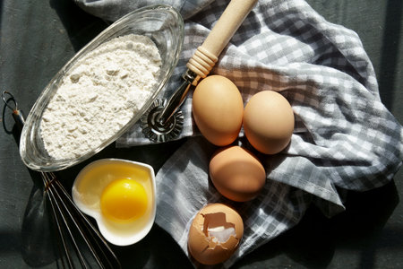 Brown eggs with flour, other tools on a grey background.