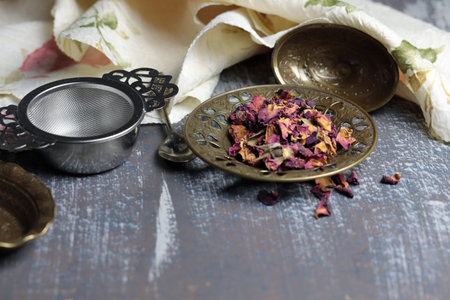 Dried Rose petals for making Rose tea in a metal container on a wooden background.