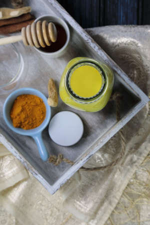 Turmeric latte, golden milk or the anti-inflammatory Indian Haldi Doodh with superfood Turmeric powder, Ginder and Cinnamon sweetened with honey on wooden background with copy space.の写真素材