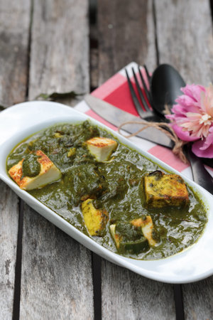 A bowl of Palak Paneer made of Paneer cheese dipped in mildly spiced Spinach gravy on wooden...
